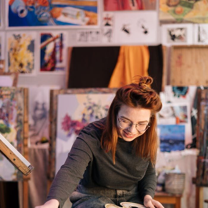 Young woman artist painting in a vibrant workshop, surrounded by art supplies and colorful paintings.