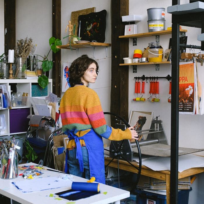A woman in a colorful sweater crafting in a well-organized artistic workshop.