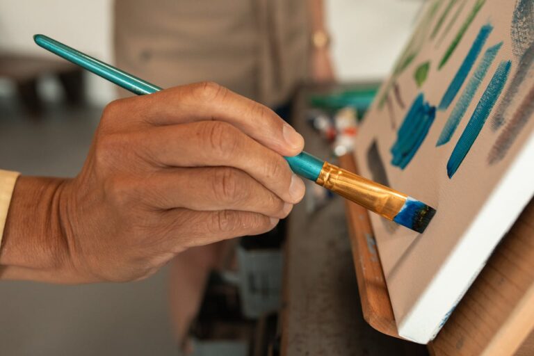 Close-up of artist's hand painting vibrant colors on canvas in studio.